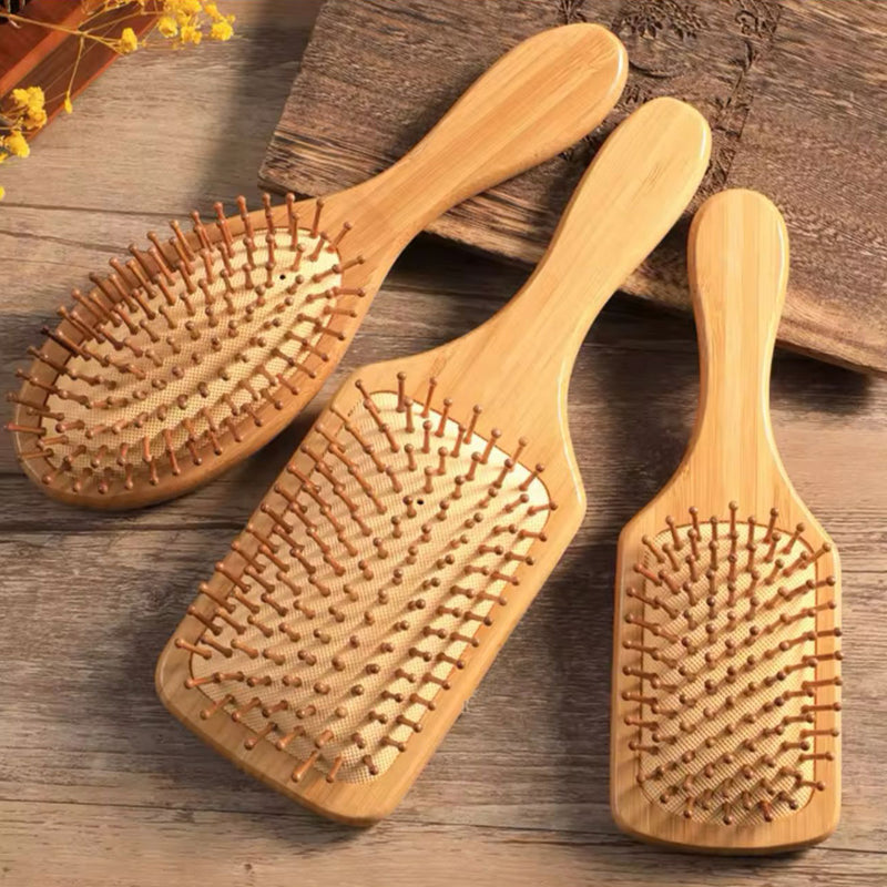 Three wooden hairbrushes with natural bristles, lying on a wooden surface.