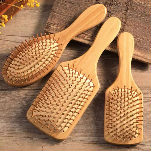 Three wooden hairbrushes with natural bristles, lying on a wooden surface.
