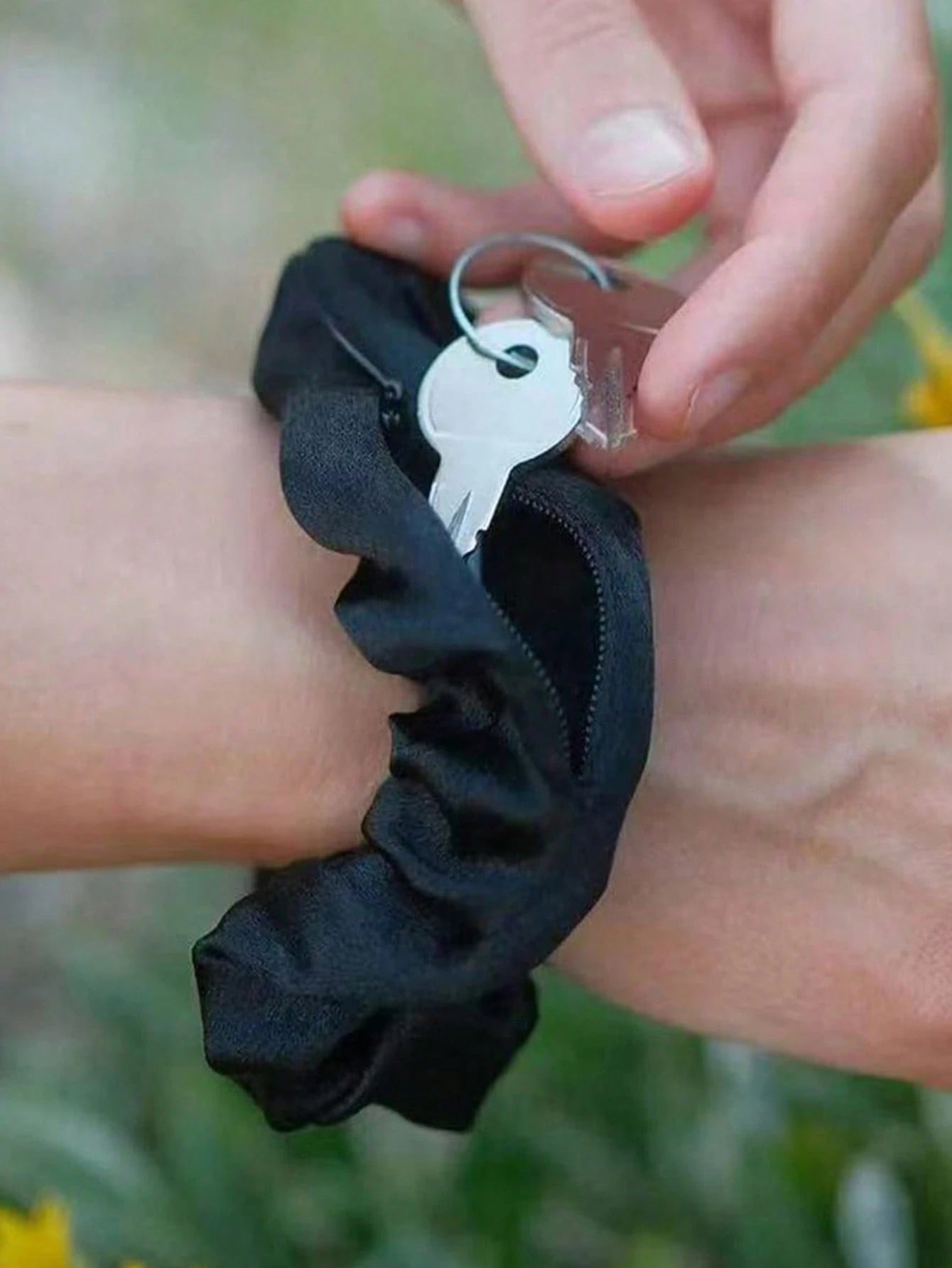 Black scrunchie on wrist with key attached, blurred natural background
